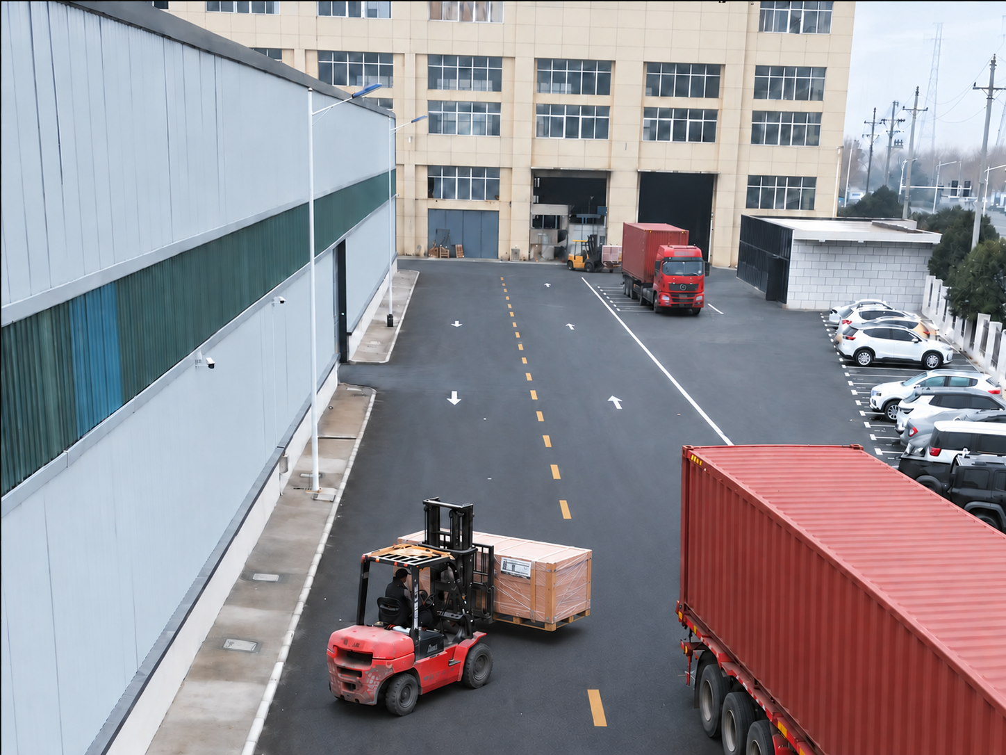 Forklift carrying a wrapped wooden packing crate toward a container truck in a factory yard